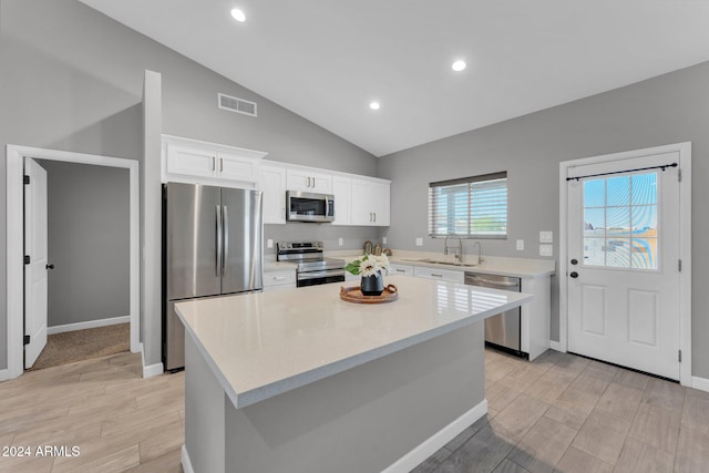 kitchen featuring lofted ceiling, white cabinetry, stainless steel appliances, light hardwood / wood-style floors, and a center island