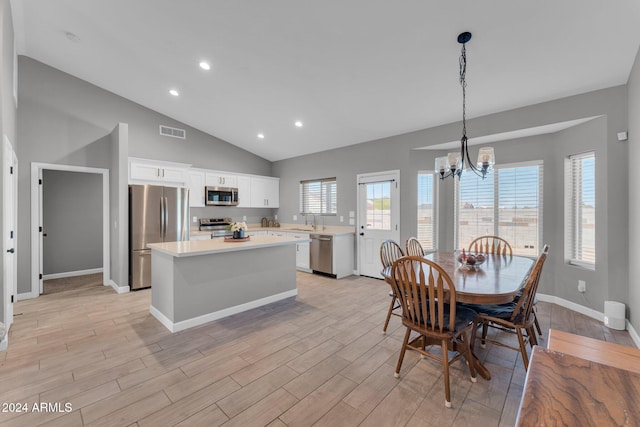 kitchen featuring a kitchen island, vaulted ceiling, pendant lighting, white cabinetry, and appliances with stainless steel finishes