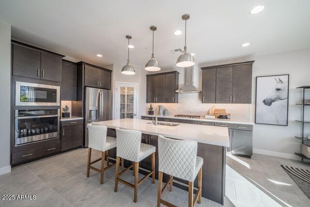 12233 W Caraveo Pl, Peoria, AZ 85383 - kitchen featuring appliances with stainless steel finishes, wall chimney exhaust hood, light countertops, dark brown cabinets, and tasteful backsplash
