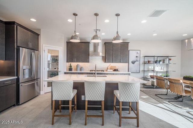 12233 W Caraveo Pl, Peoria, AZ 85383 - kitchen featuring stainless steel fridge with ice dispenser, wall chimney exhaust hood, light countertops, dark brown cabinetry, and recessed lighting