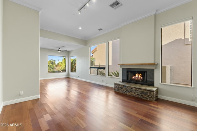 unfurnished living room with rail lighting, ceiling fan, hardwood / wood-style floors, a fireplace, and ornamental molding