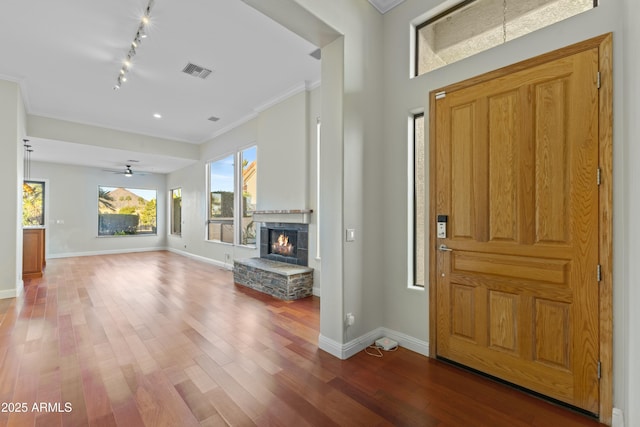 entrance foyer with a stone fireplace, track lighting, ornamental molding, and hardwood / wood-style flooring