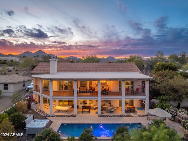 back house at dusk featuring a pool with hot tub, a patio, central AC unit, and a balcony