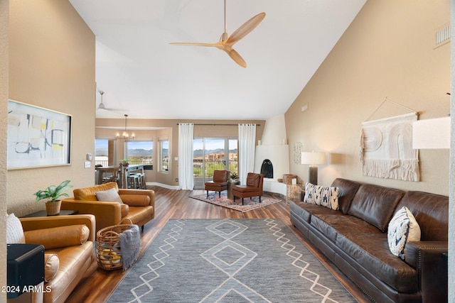 living room with dark wood-type flooring, ceiling fan with notable chandelier, and high vaulted ceiling