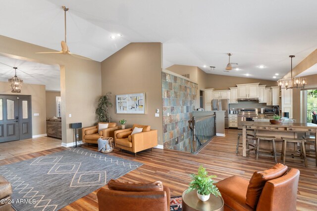 living room featuring light hardwood / wood-style floors, ceiling fan with notable chandelier, and vaulted ceiling