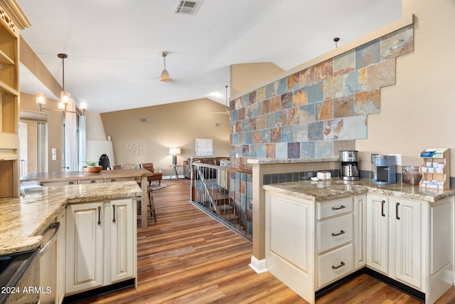 kitchen featuring light stone countertops, wood-type flooring, decorative light fixtures, and vaulted ceiling