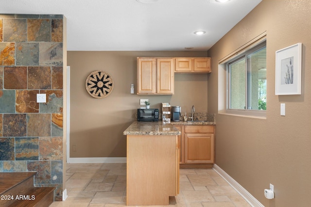 kitchen with light brown cabinetry, sink, and light stone countertops