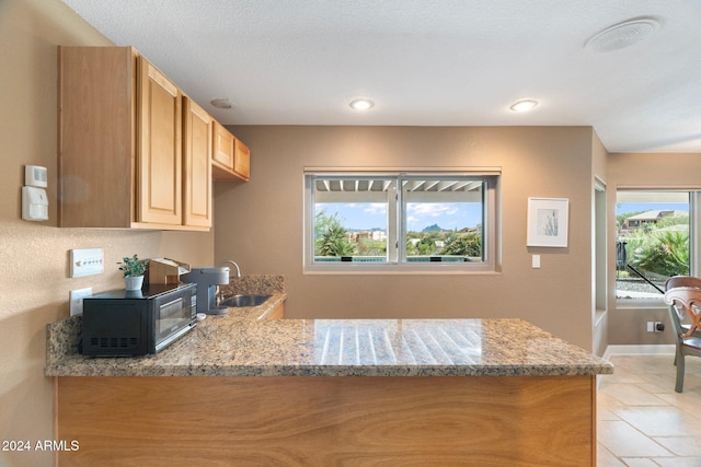 kitchen with light brown cabinetry, kitchen peninsula, sink, and light stone counters