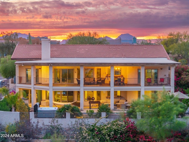 back house at dusk featuring a balcony and a patio