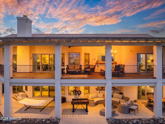 back house at dusk with a balcony, a patio, and an outdoor living space