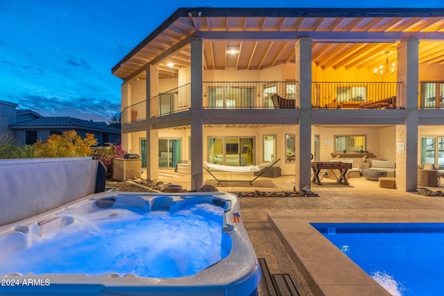 back house at dusk with an outdoor hangout area, a patio area, a swimming pool with hot tub, and a balcony