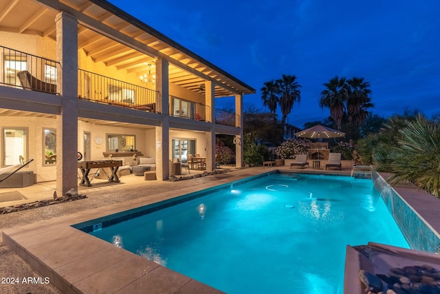 pool at twilight featuring a patio area, outdoor lounge area, and pool water feature