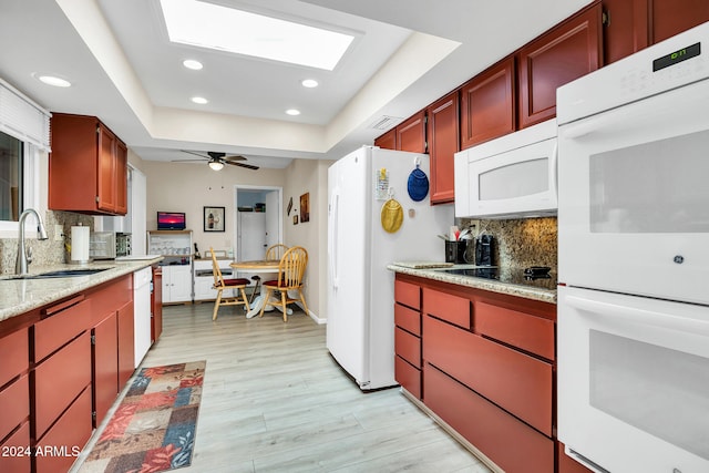 kitchen with tasteful backsplash, white appliances, a tray ceiling, sink, and light hardwood / wood-style floors