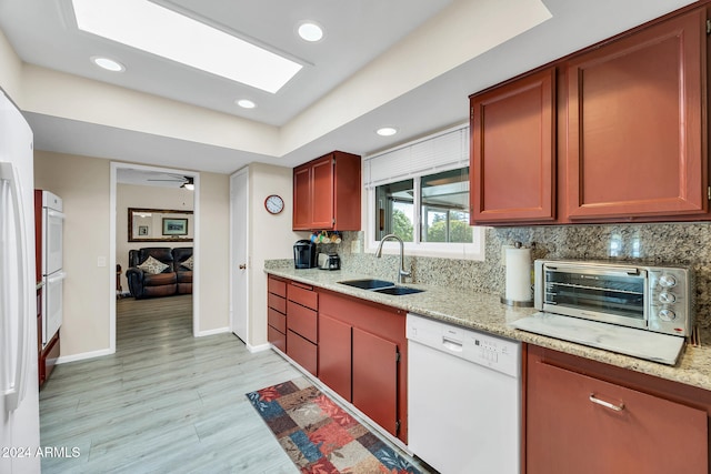 kitchen featuring white dishwasher, sink, decorative backsplash, light wood-type flooring, and light stone counters