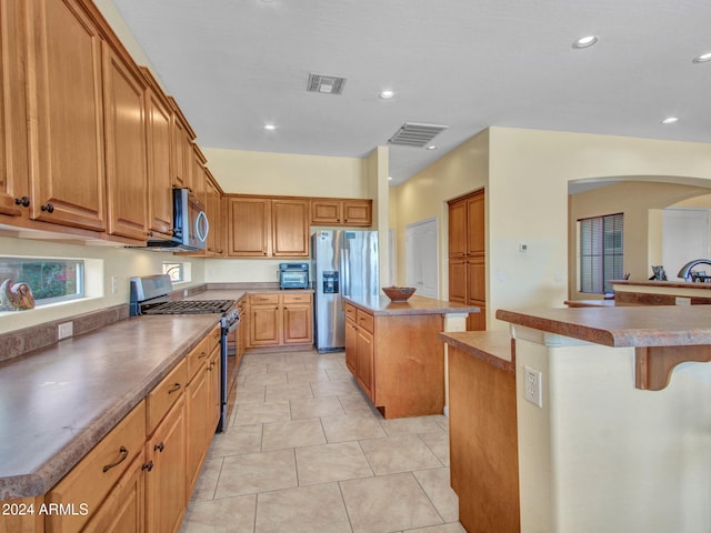 kitchen with a kitchen island, appliances with stainless steel finishes, light tile patterned floors, and a breakfast bar