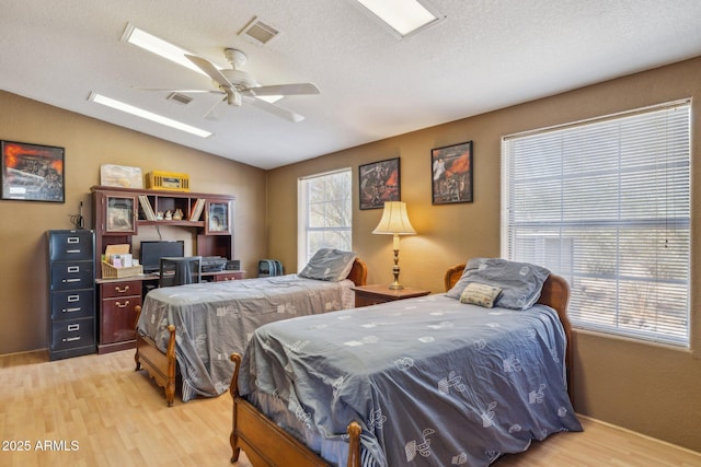 bedroom with visible vents, a ceiling fan, light wood-style flooring, vaulted ceiling, and a textured ceiling