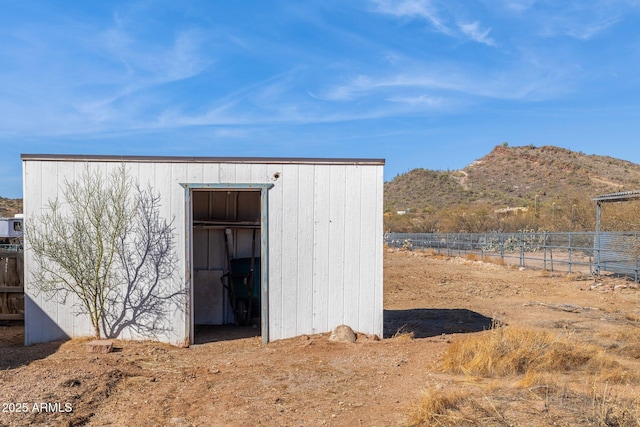 view of outdoor structure featuring fence, a mountain view, and an outbuilding