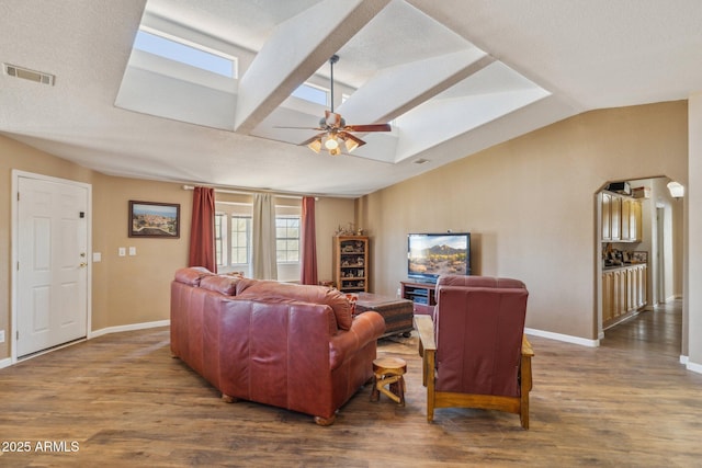 living area with wood finished floors, visible vents, baseboards, a ceiling fan, and lofted ceiling with skylight