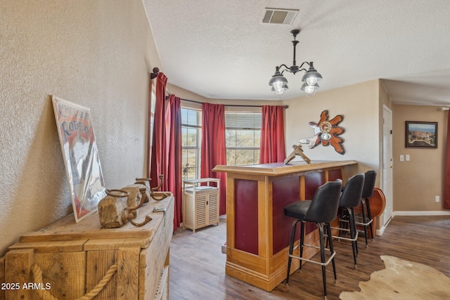 kitchen featuring a chandelier, a textured ceiling, wood finished floors, visible vents, and baseboards