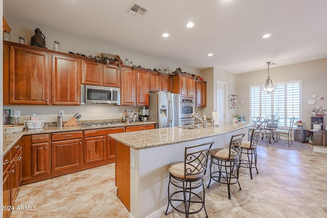 kitchen featuring a center island with sink, a kitchen breakfast bar, decorative light fixtures, light stone counters, and stainless steel appliances