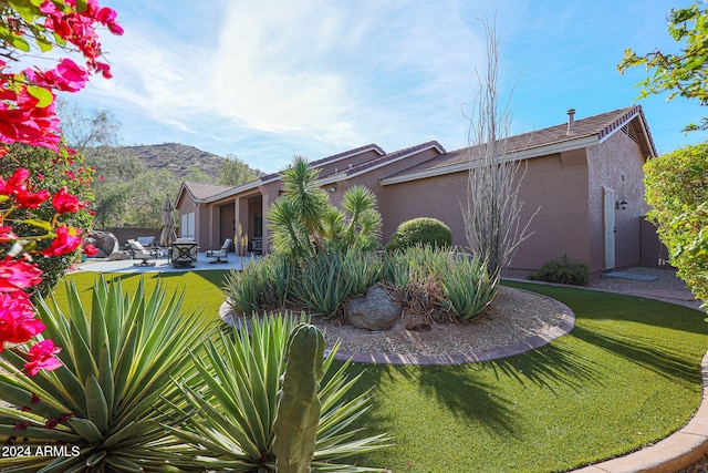 view of side of home featuring a lawn, a mountain view, and a patio