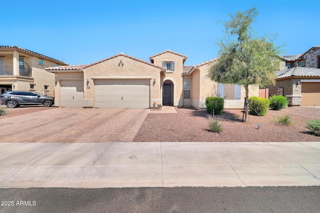 mediterranean / spanish-style home featuring a tile roof, a garage, decorative driveway, and stucco siding