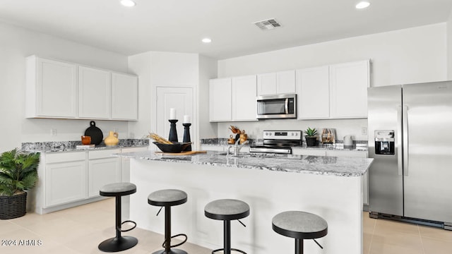 kitchen with light stone counters, appliances with stainless steel finishes, visible vents, and a kitchen breakfast bar