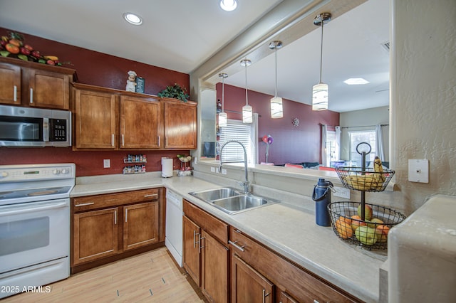kitchen featuring white appliances, light countertops, brown cabinets, a sink, and light wood finished floors