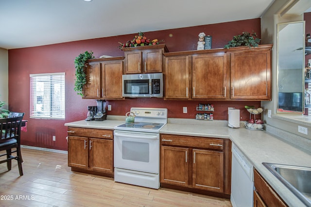 kitchen with a sink, white appliances, light countertops, brown cabinetry, and light wood-type flooring