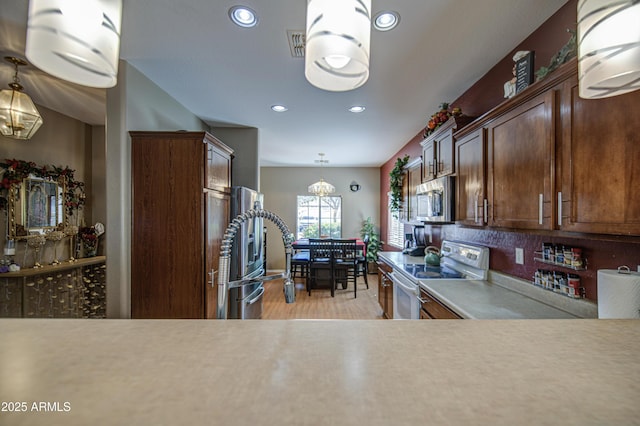 kitchen with light countertops, tasteful backsplash, light wood-style flooring, appliances with stainless steel finishes, and decorative light fixtures
