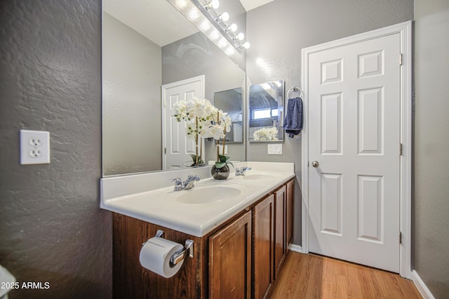 bathroom featuring a sink, a textured wall, double vanity, and wood finished floors