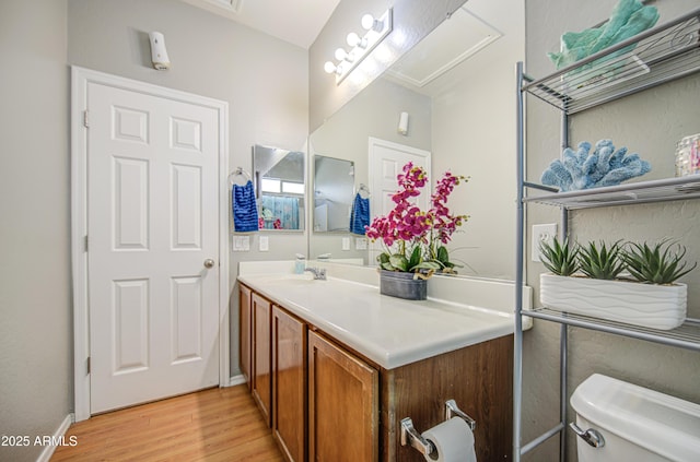 half bath with toilet, baseboards, wood finished floors, and vanity