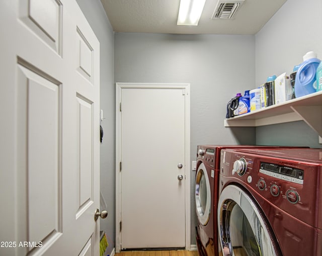 washroom featuring laundry area, washing machine and dryer, wood finished floors, and visible vents