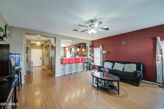 living area with visible vents, an accent wall, wood finished floors, baseboards, and ceiling fan