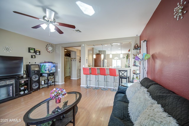 living room with a ceiling fan, visible vents, and wood finished floors