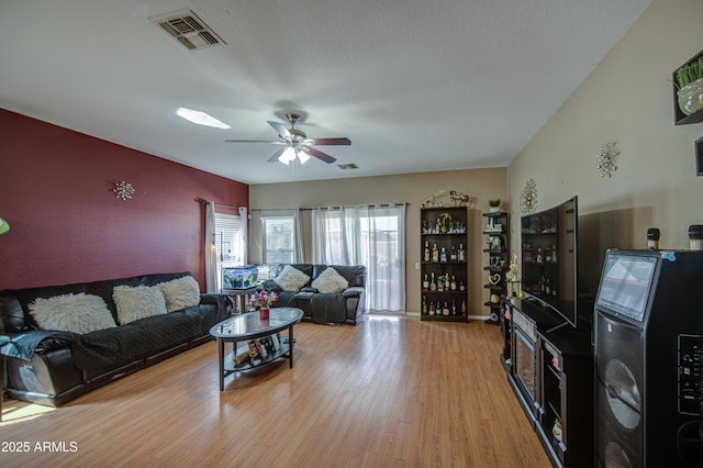 living area featuring visible vents, a ceiling fan, light wood finished floors, and an accent wall