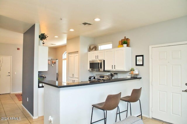 kitchen featuring kitchen peninsula, appliances with stainless steel finishes, light tile patterned floors, and white cabinetry