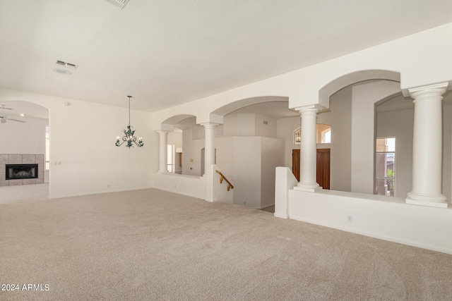 empty room featuring carpet floors, visible vents, a ceiling fan, a tile fireplace, and ornate columns