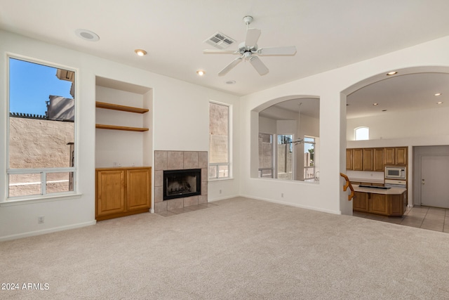 unfurnished living room with ceiling fan, a tiled fireplace, and light colored carpet