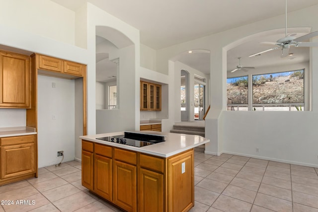 kitchen with light tile patterned floors, a kitchen island, brown cabinets, black electric stovetop, and light countertops