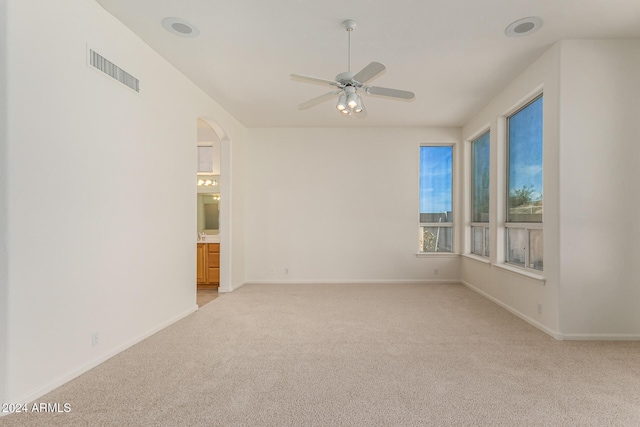 spare room with arched walkways, visible vents, a ceiling fan, light carpet, and baseboards