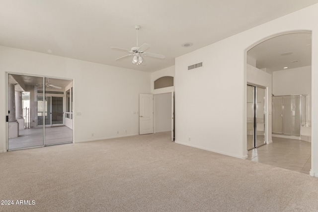 empty room with carpet floors, visible vents, arched walkways, and a ceiling fan