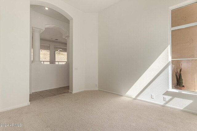 carpeted spare room featuring arched walkways, decorative columns, and baseboards