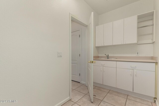 kitchen featuring baseboards, light countertops, white cabinetry, a sink, and light tile patterned flooring