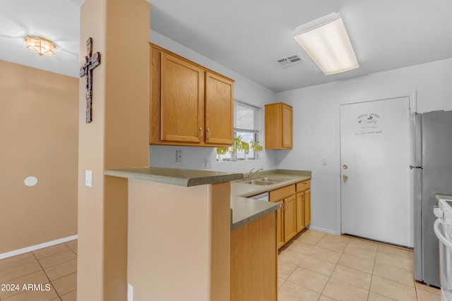 kitchen with light tile patterned floors, stove, stainless steel refrigerator, and sink