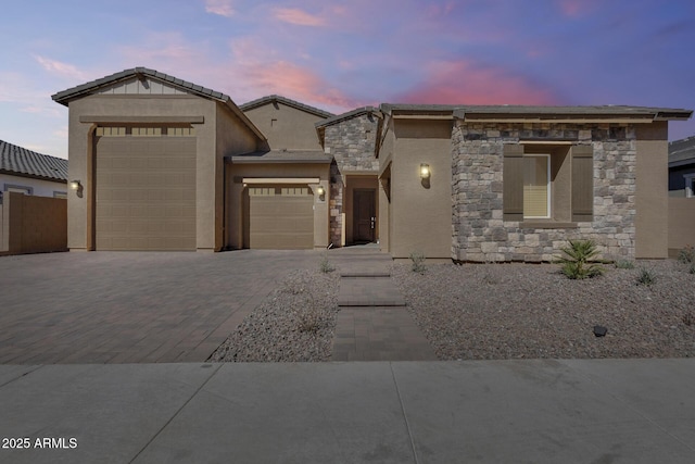 view of front of property with a garage, decorative driveway, stone siding, and stucco siding