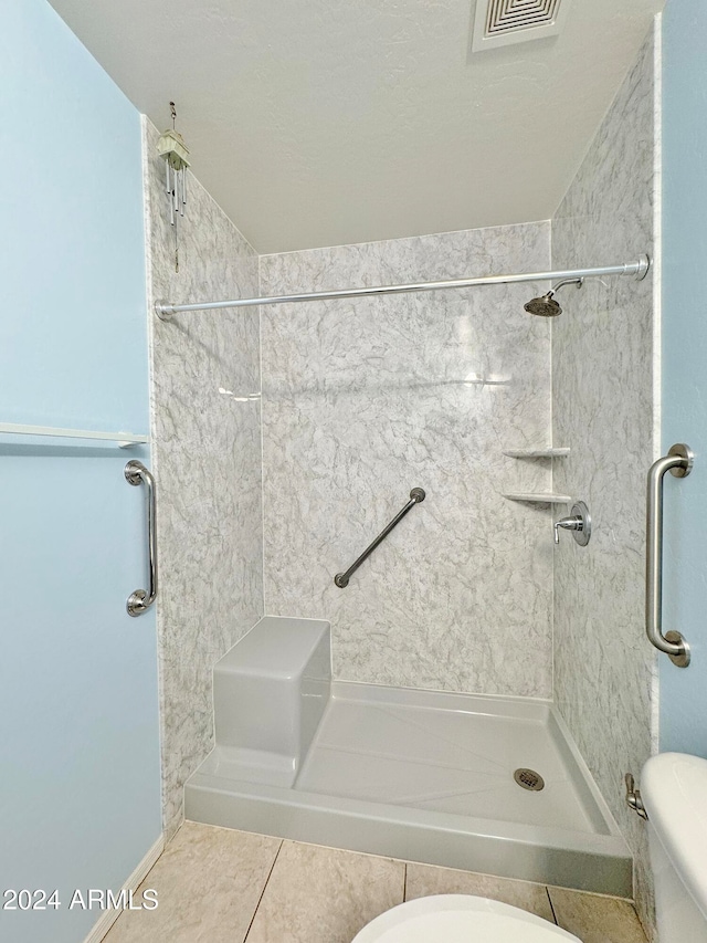 bathroom with tile patterned flooring, toilet, and a tile shower