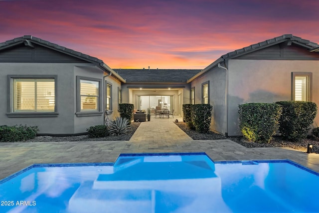 rear view of property with an outdoor pool, stucco siding, and a patio