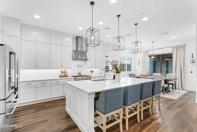 kitchen featuring visible vents, high end fridge, wall chimney exhaust hood, and a sink