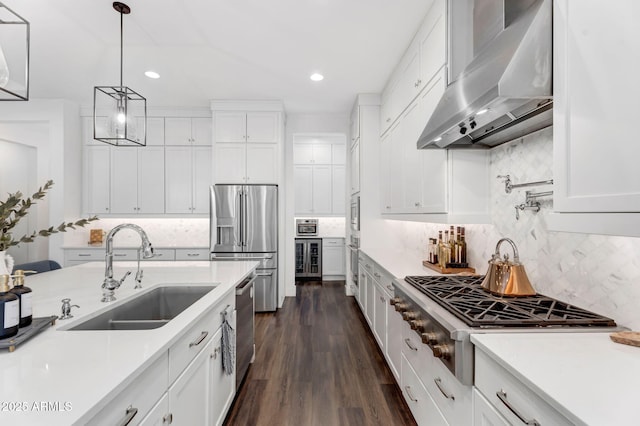 kitchen with wall chimney range hood, light countertops, stainless steel appliances, white cabinetry, and a sink